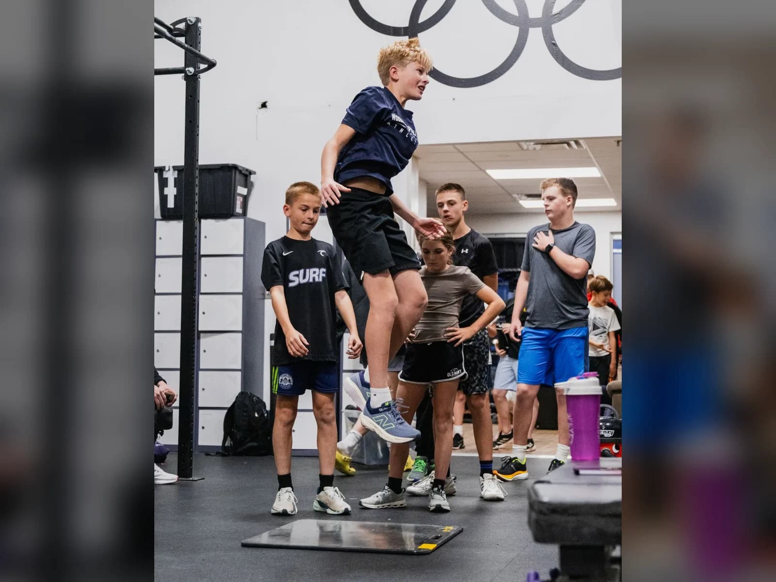 An athlete in mid-air above the jump plate while teammates watch