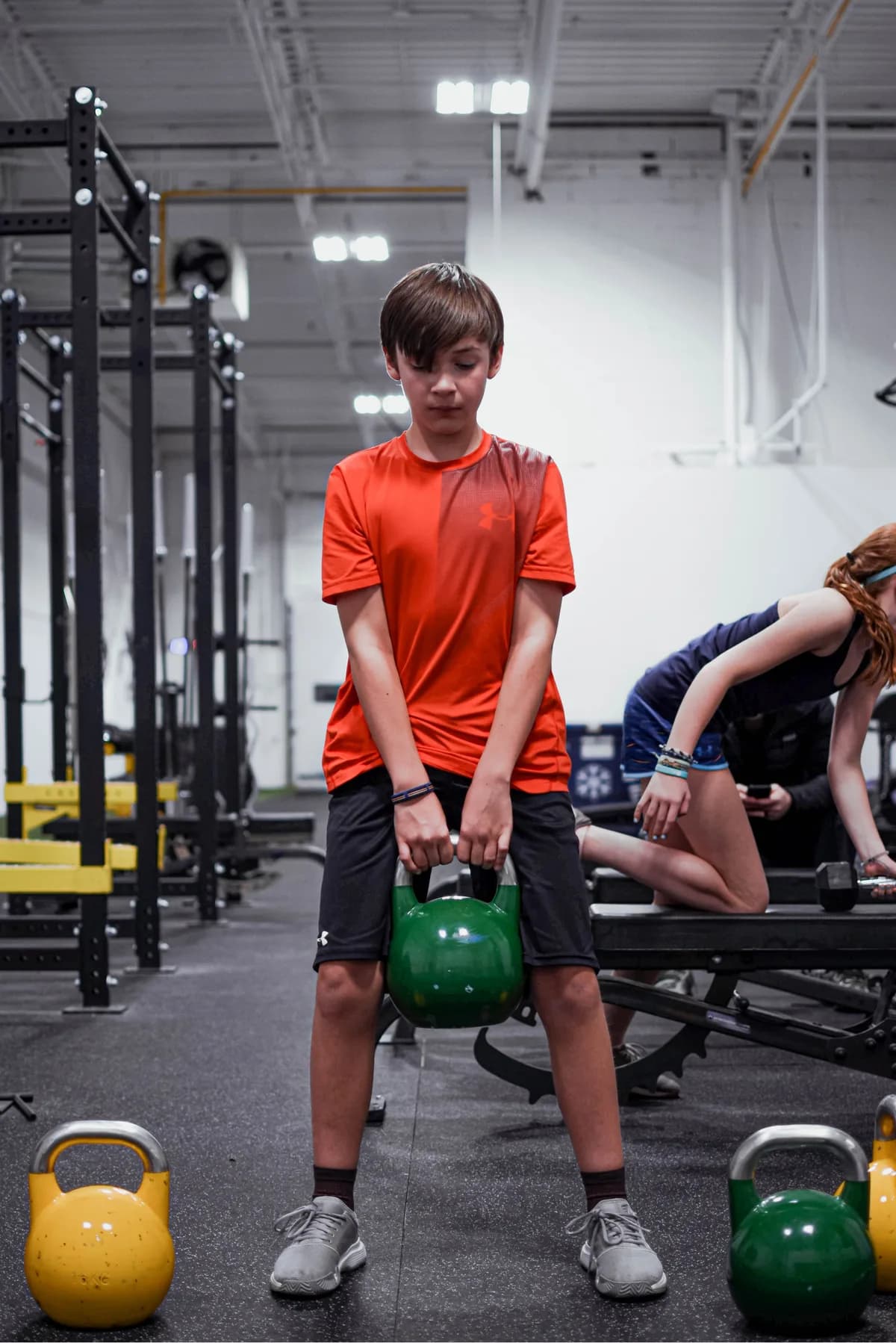 A youth athlete in a red shirt practising a kettlebell lift at CANAM